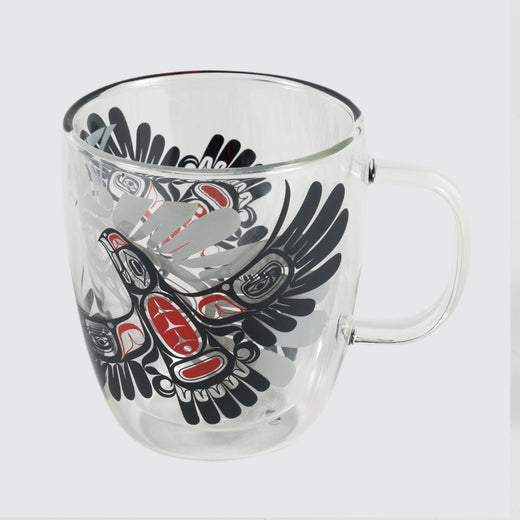 Une tasse transparente avec des aigles noirs et rouges imprimés à l’extérieur et l’ombre d’un plus gros aigle imprimée à l’intérieur.