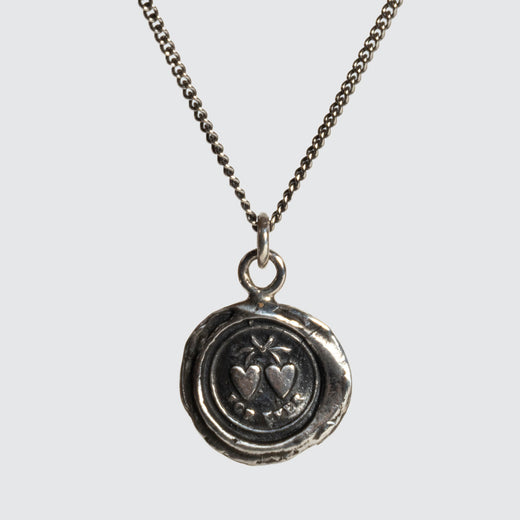 Un pendentif en argent décoré de deux cœurs et du mot « Forever », suspendu à une chaîne. 