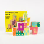 Blocs de bois de couleurs pastel devant une boîte sur laquelle on peut lire, en anglais, « Blockitecture® Deco Architect Building Blocks »