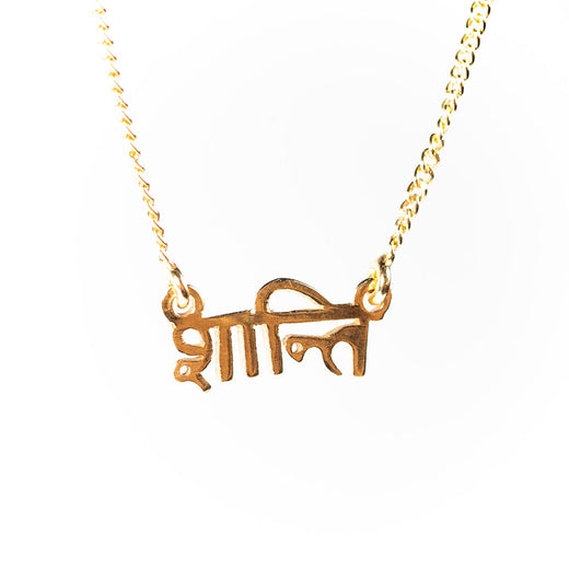 Pendentif doré sur une chaîne; le pendentif est le mot « shanti » en sanskrit.