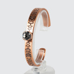 Un bracelet en cuivre orné d’un motif de plume et incrusté d’un cristal de verre, vu d’un angle. 